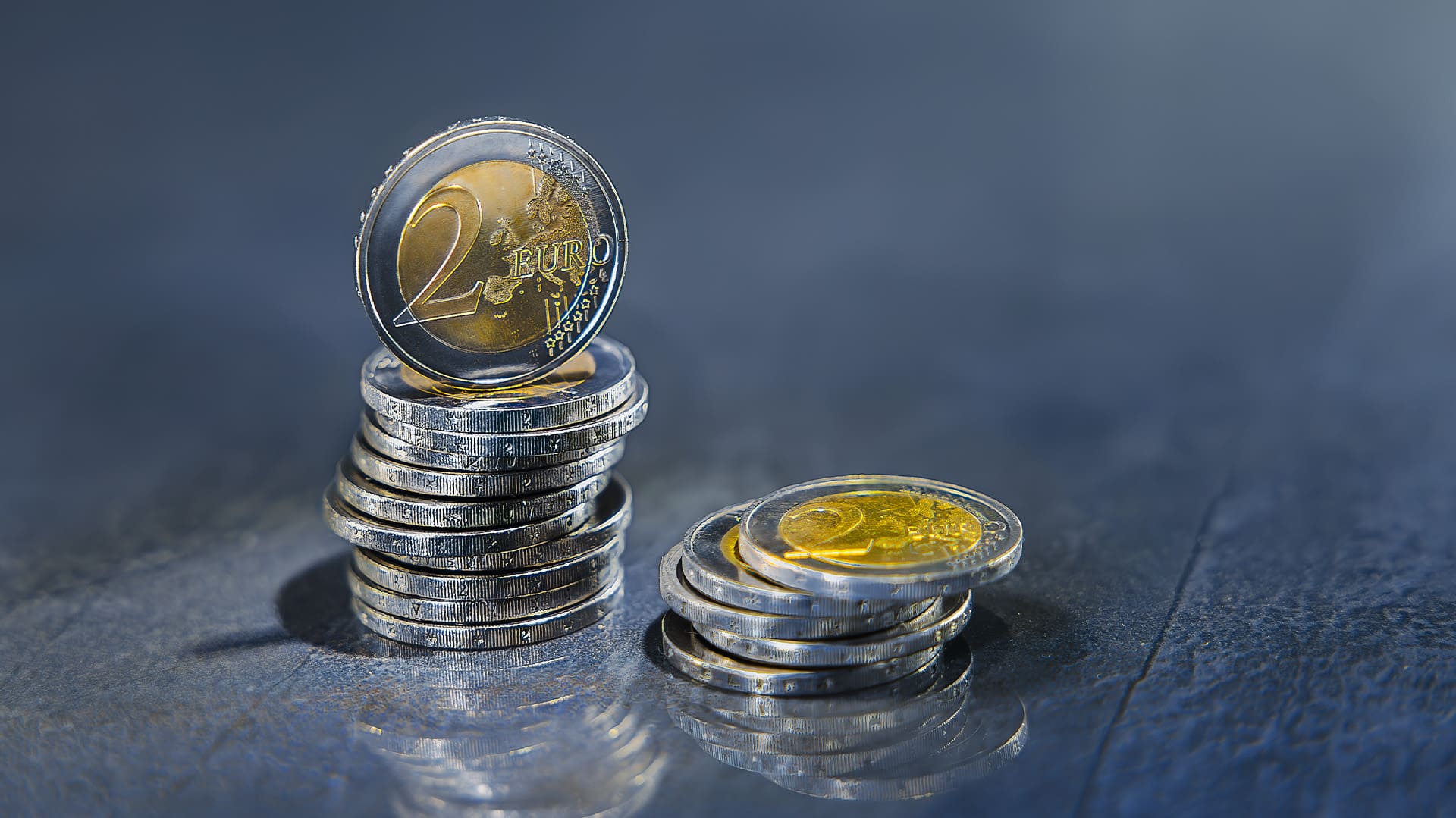 Nahaufnahme von zwei Stapeln mit 2-Euro-Münzen liegen nebeneinander auf einem dunklen Hintergrund Nahaufnahme von zwei Stapeln mit 2-Euro-Münzen liegen nebeneinander auf einem dunklen Hintergrund