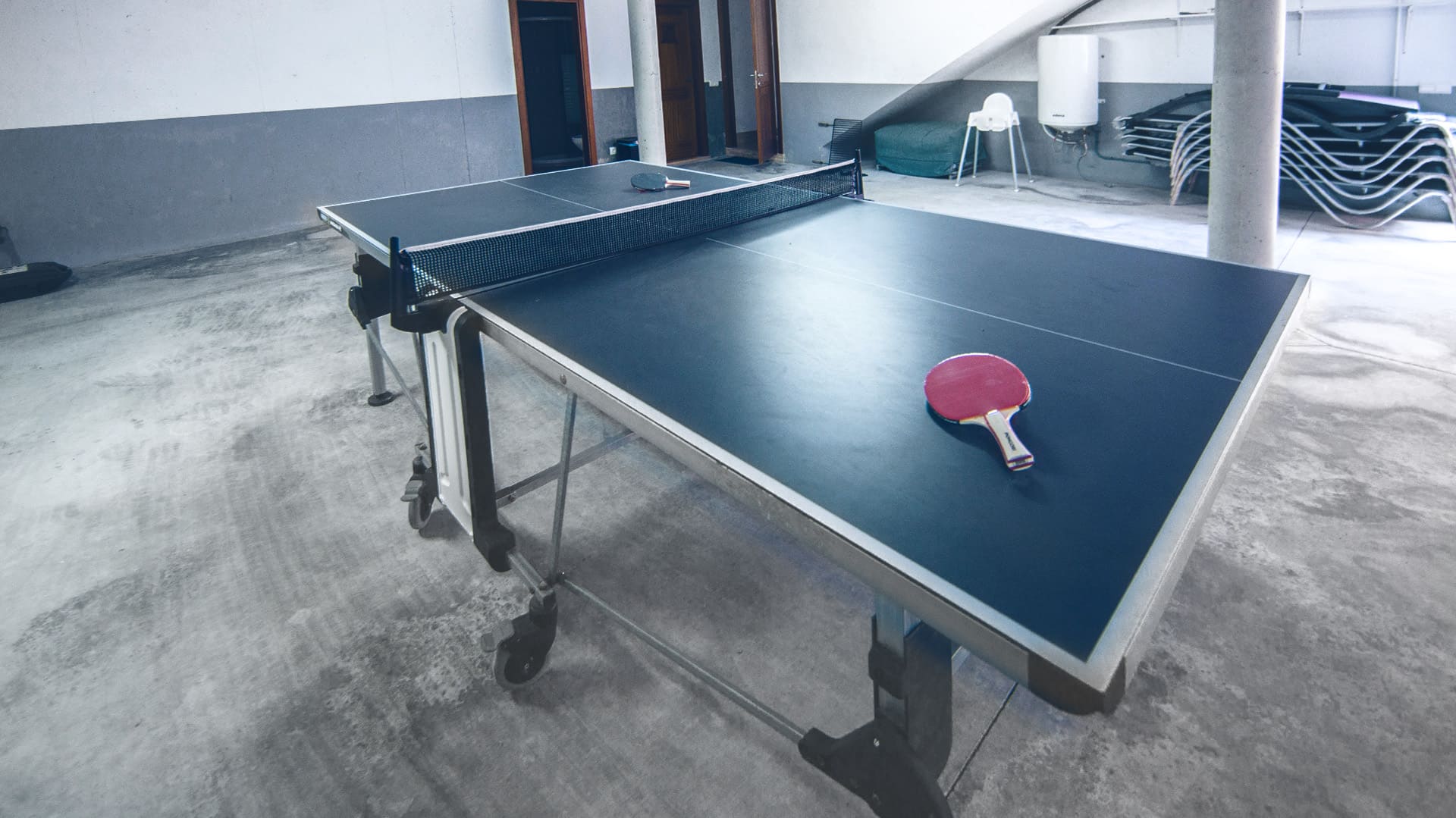 Eine Tischtennisplatte mit Tischtennisschlägern in einem Keller Eine Tischtennisplatte mit Tischtennisschlägern in einem Keller