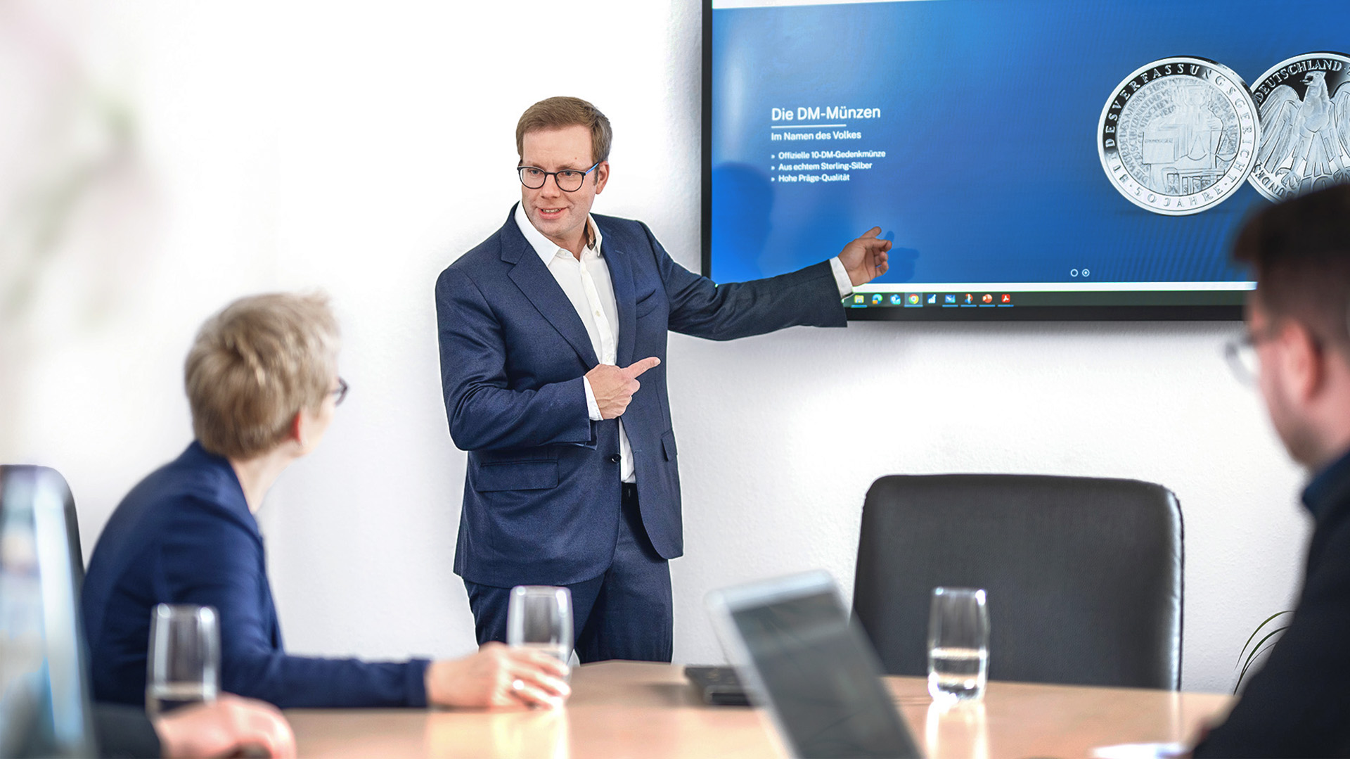 Ein Geschäftsführer zeigt während einer Konferenz auf einen Bildschirm an der Wand Ein Geschäftsführer zeigt während einer Konferenz auf einen Bildschirm an der Wand