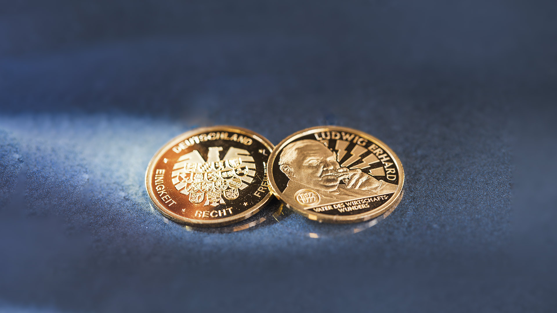 Die Gold-Gedenkprägung Ludwig Erhard liegt auf blau-grauen Hintergrund Die Gold-Gedenkprägung Ludwig Erhard liegt auf blau-grauen Hintergrund