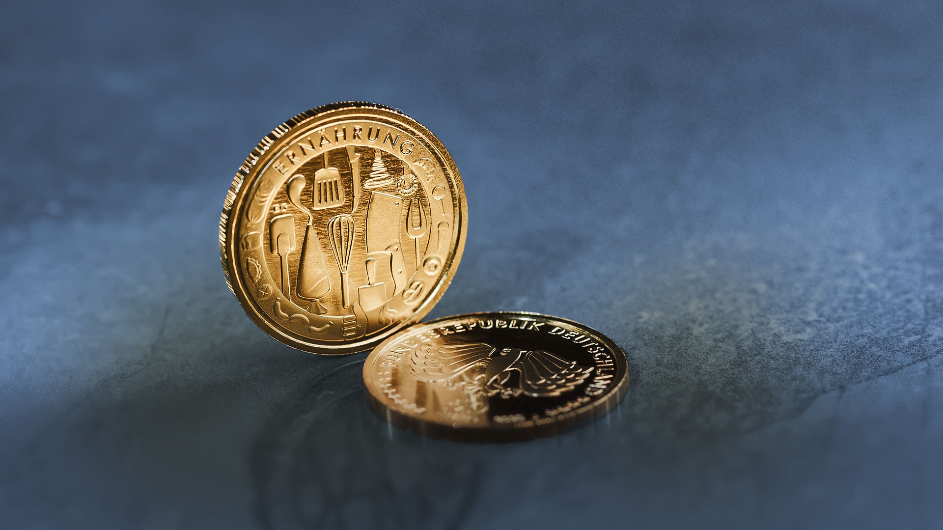 Die 50-Euro-Goldmünze Ernährung steht vor blau-grauen Hintergrund Die 50-Euro-Goldmünze Ernährung steht vor blau-grauen Hintergrund