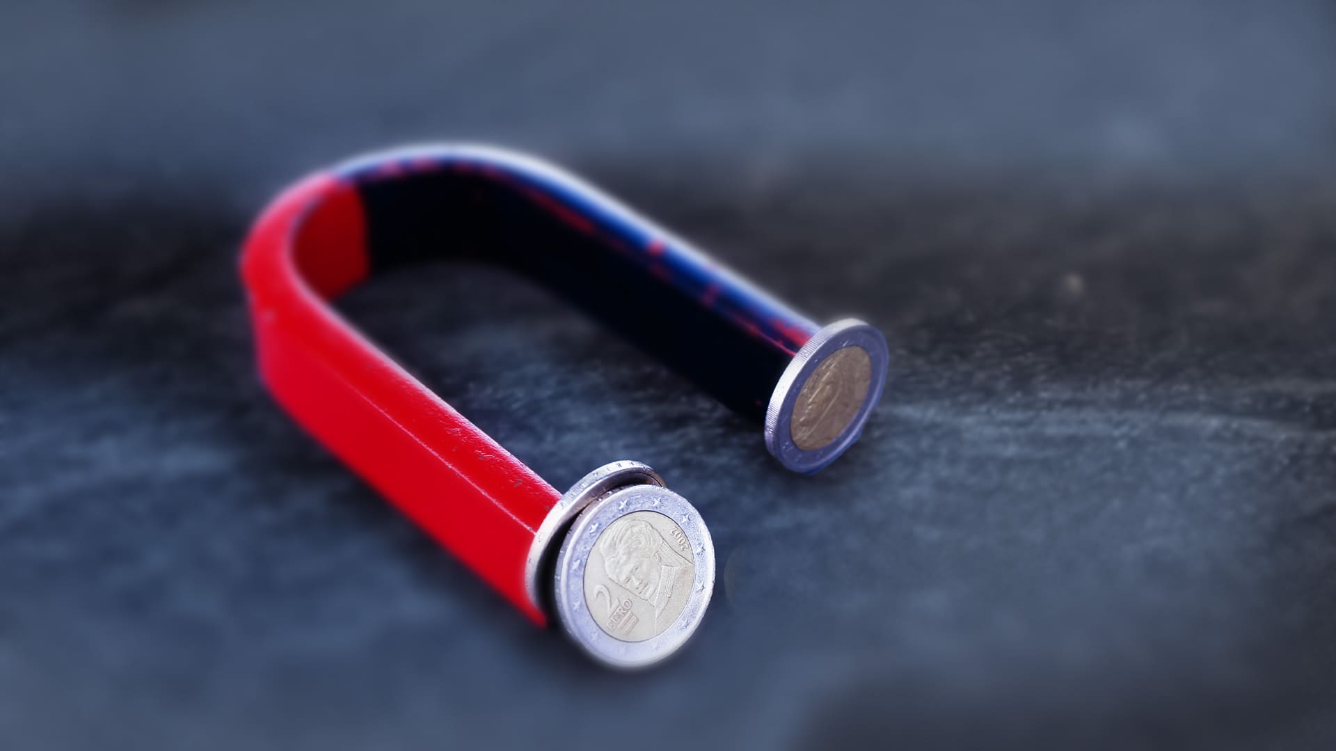 Roter Magnet mit mehreren 2-Euro-Münzen an den Enden des Magnets auf einem dunklen Hintergrund Roter Magnet mit mehreren 2-Euro-Münzen an den Enden des Magnets auf einem dunklen Hintergrund
