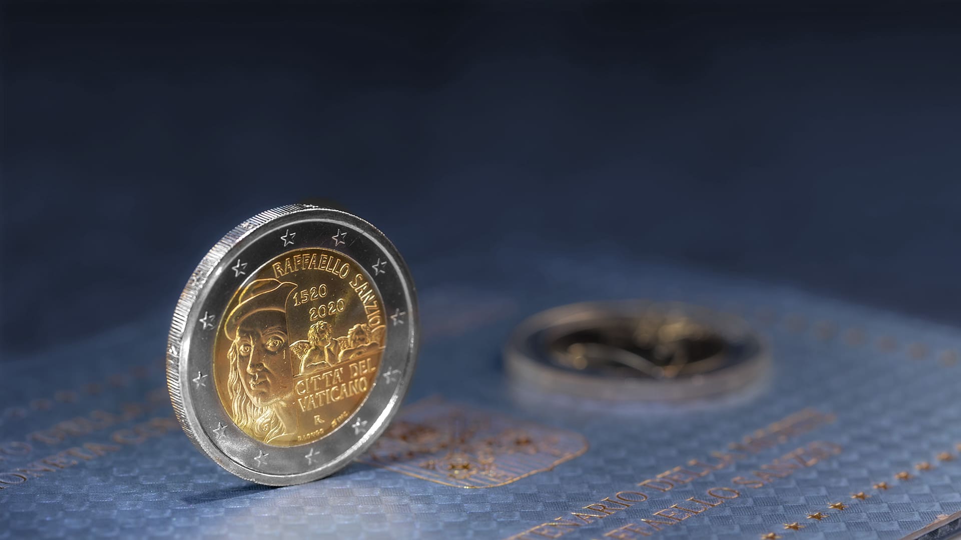 2-Euro-Gedenkmünze-Vatikan zum 500. Todestag von Raffaello Sanzio aus dem Jahr 2020 steht vor blau-grauen Hintergrund 2-Euro-Gedenkmünze-Vatikan zum 500. Todestag von Raffaello Sanzio aus dem Jahr 2020 steht vor blau-grauen Hintergrund