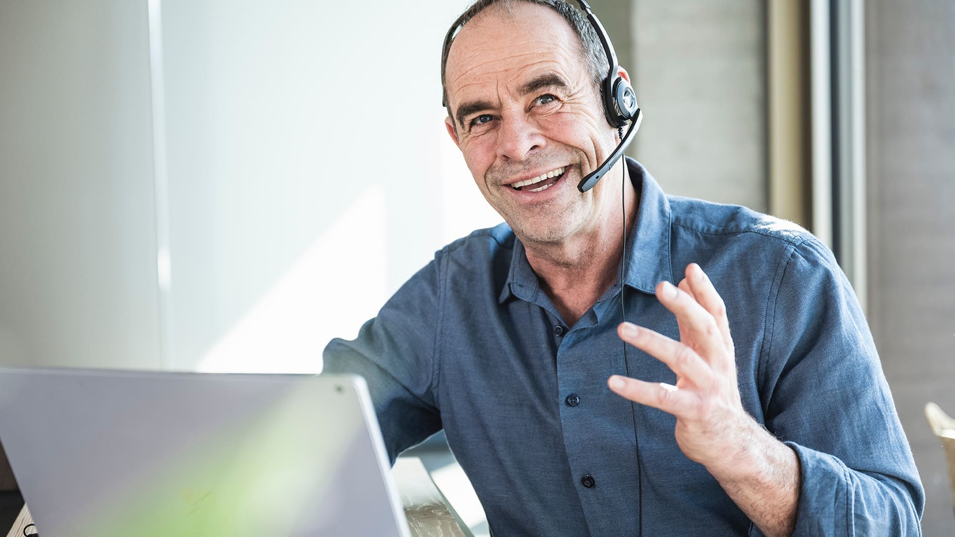Ein Kundenservice-Mitarbeiter mit Headset sitzt vor einem Laptop und führt ein Gespräch Ein Kundenservice-Mitarbeiter mit Headset sitzt vor einem Laptop und führt ein Gespräch