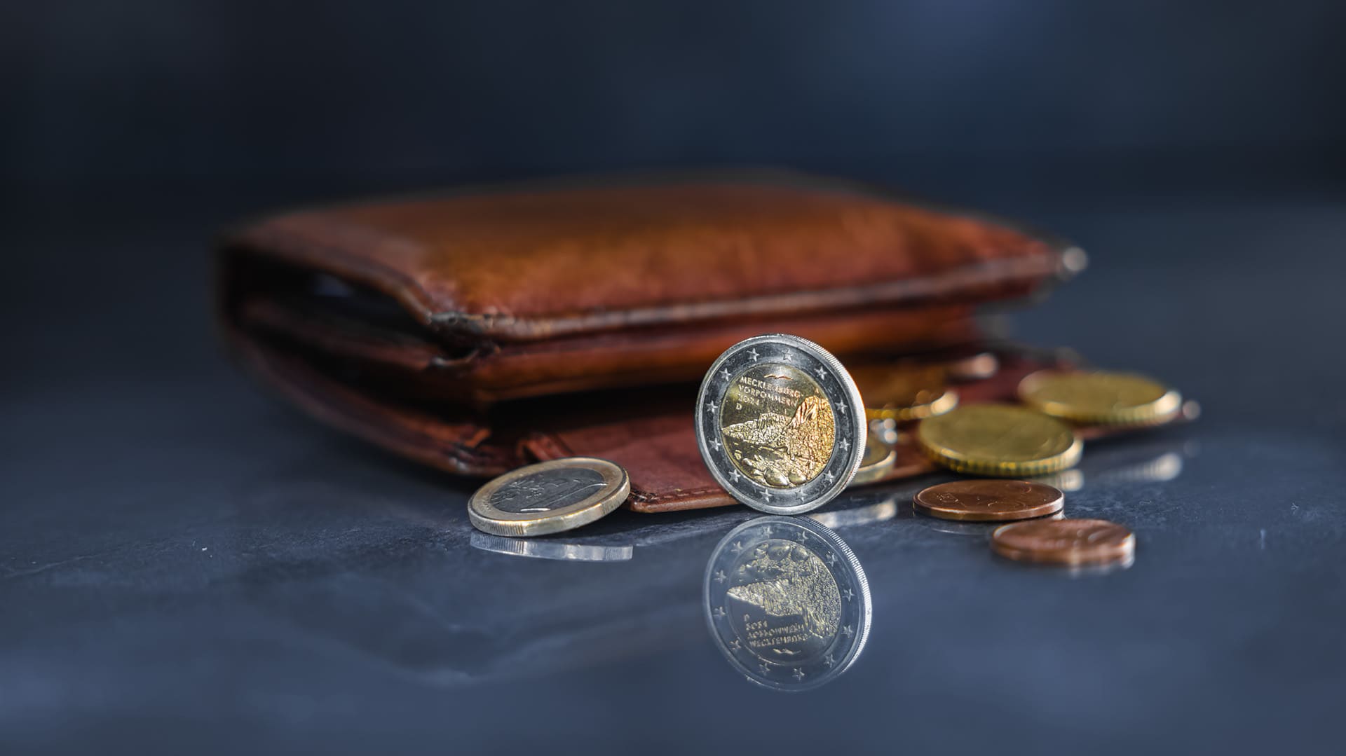 Nahaufnahme von einem dunkelbraunen Portemonnaie mit unterschiedlichen Euro-Kursmünzen auf einem dunklen Hintergrund Nahaufnahme von einem dunkelbraunen Portemonnaie mit unterschiedlichen Euro-Kursmünzen auf einem dunklen Hintergrund