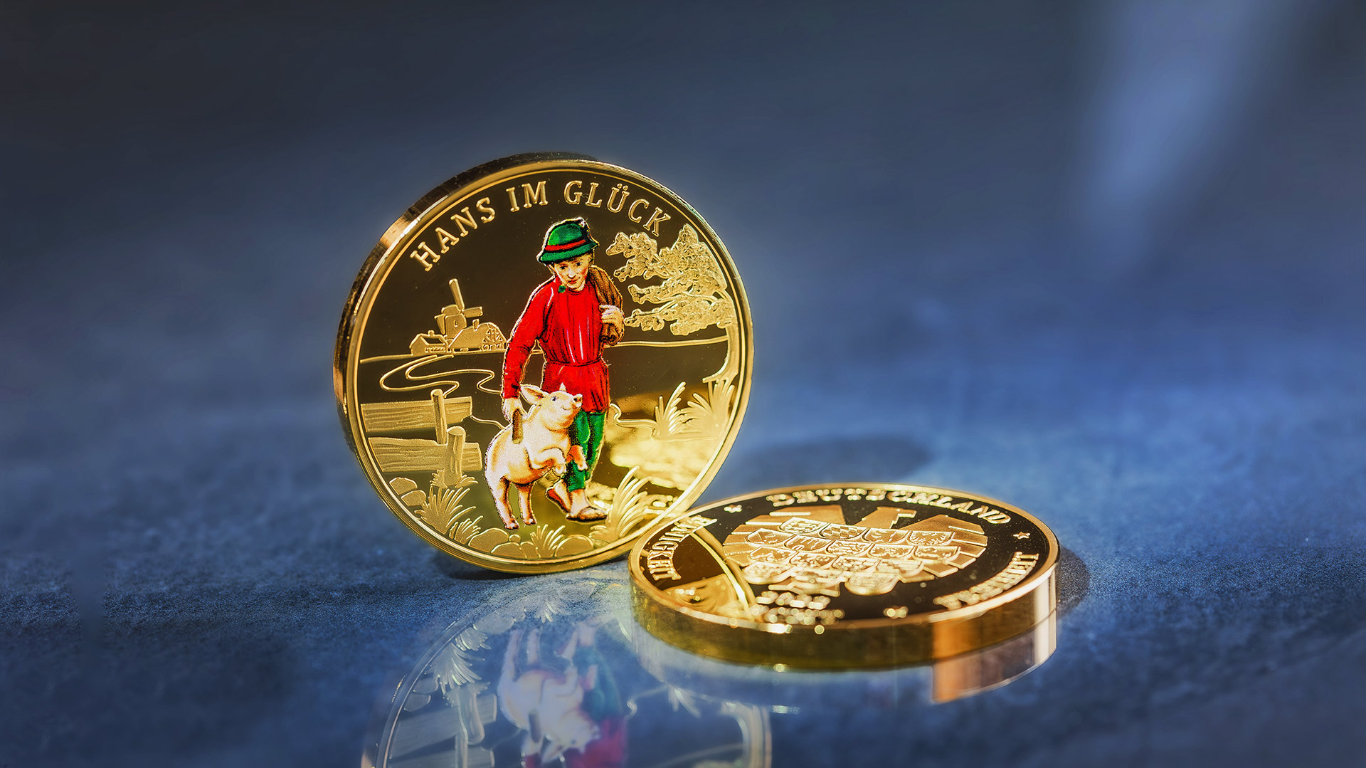 Die Piedfort-Gedenkprägung Hans im Glück steht vor blau-grauen Hintergrund Die Piedfort-Gedenkprägung Hans im Glück steht vor blau-grauen Hintergrund
