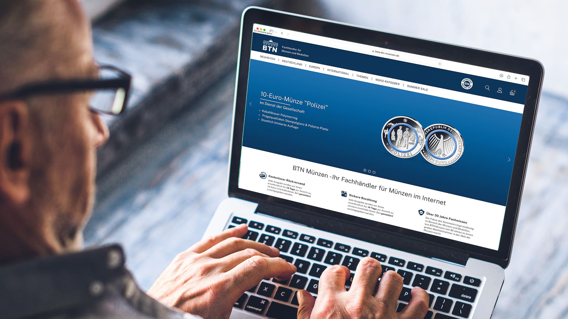 Ein älterer Mann mit Brille schaut sich die Homepage von BTN Münzen an und tippt auf der Laptoptastatur mit seinen Händen Ein älterer Mann mit Brille schaut sich die Homepage von BTN Münzen an und tippt auf der Laptoptastatur mit seinen Händen