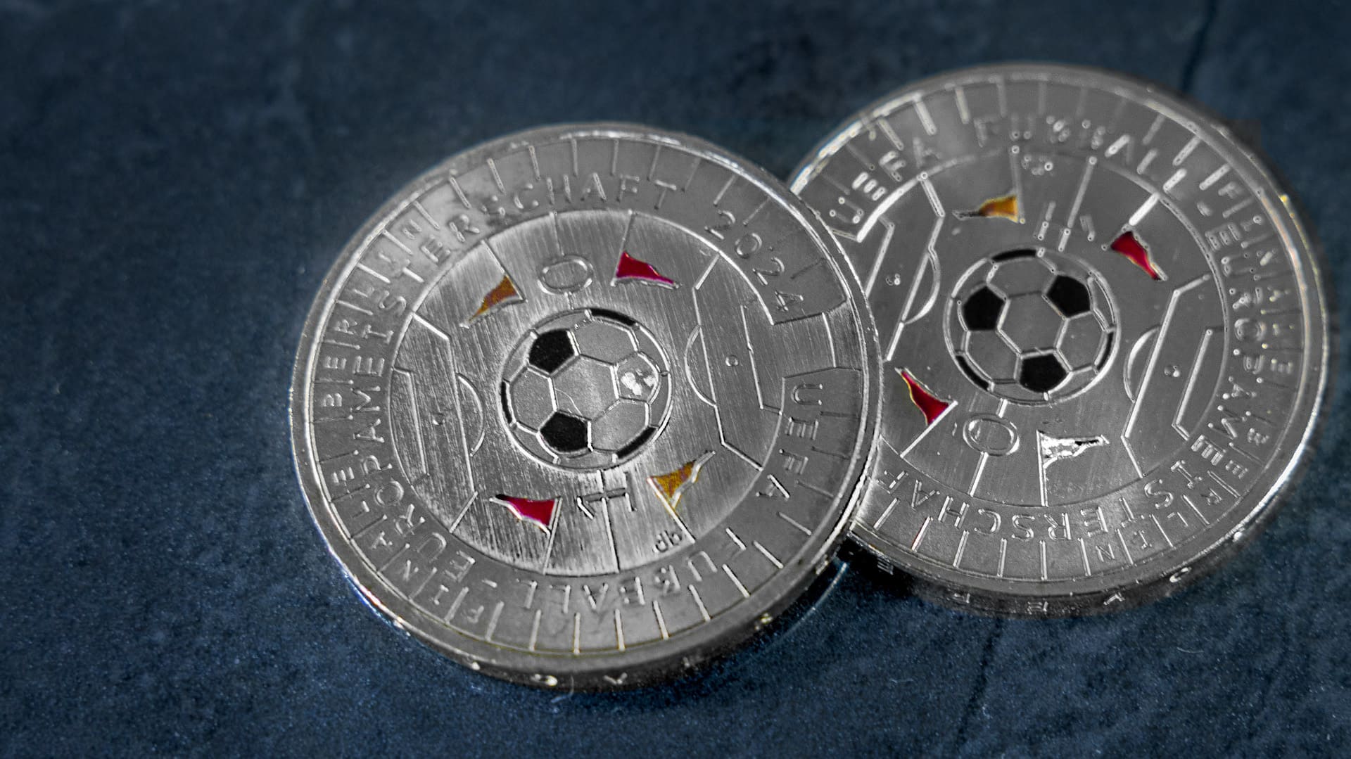 Zwei ungleiche 11-Euro-Münzen zur Fußball-EM 2024 liegen vor blau-grauen Hintergrund Zwei ungleiche 11-Euro-Münzen zur Fußball-EM 2024 liegen vor blau-grauen Hintergrund