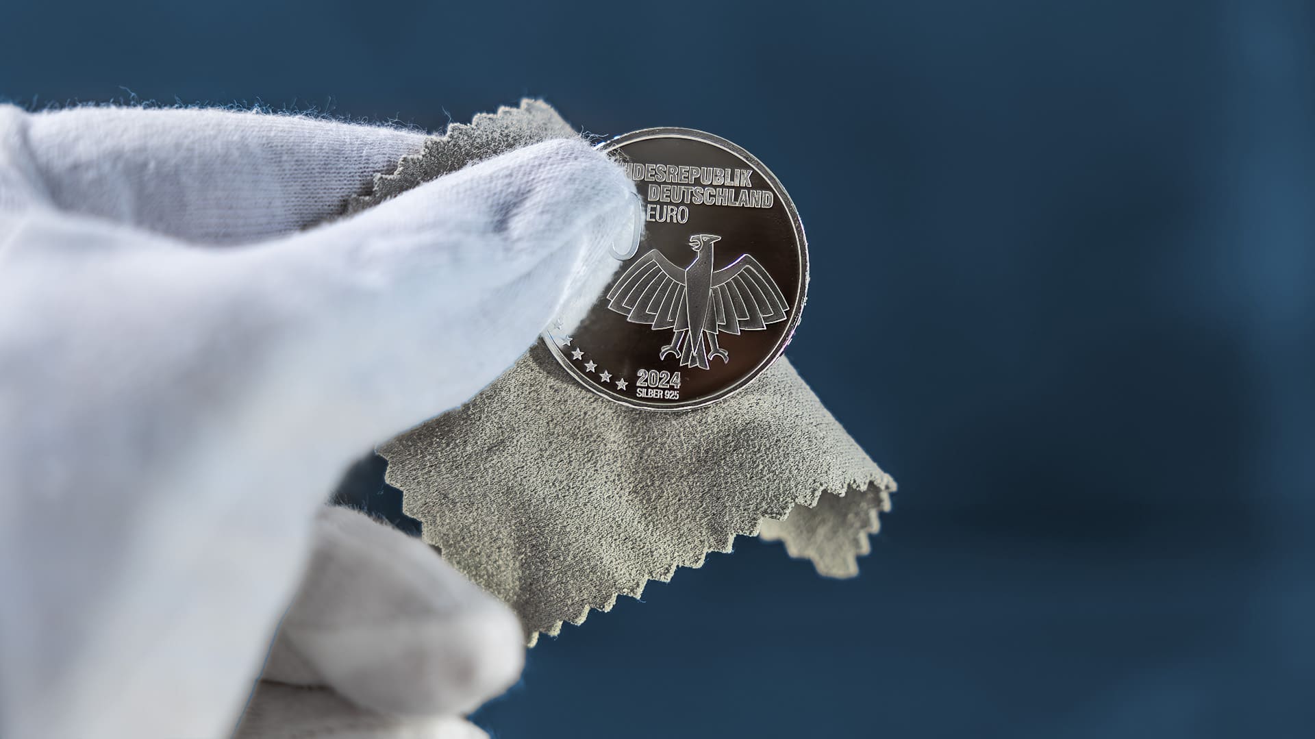 Hand mit Handschuh hält Münze und Poliertuch Hand mit Handschuh hält Münze und Poliertuch