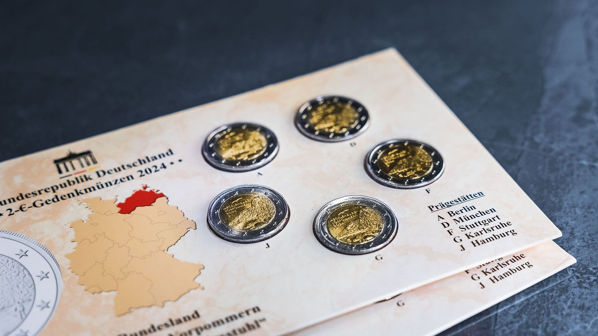 2-Euro-Gedenkmünzensatz in Blisterverpackung vor blau-grauen Hintergrund 2-Euro-Gedenkmünzensatz in Blisterverpackung vor blau-grauen Hintergrund