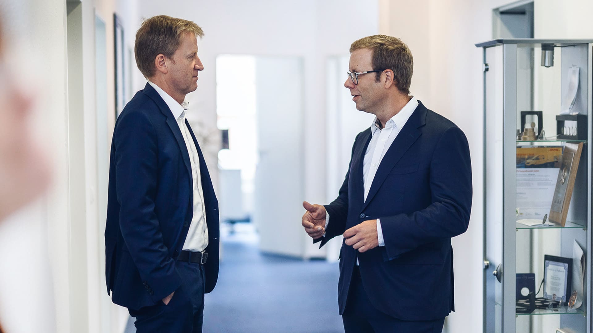 Zwei Geschäftsführer in Anzug unterhalten sich auf einem Büroflur Zwei Geschäftsführer in Anzug unterhalten sich auf einem Büroflur