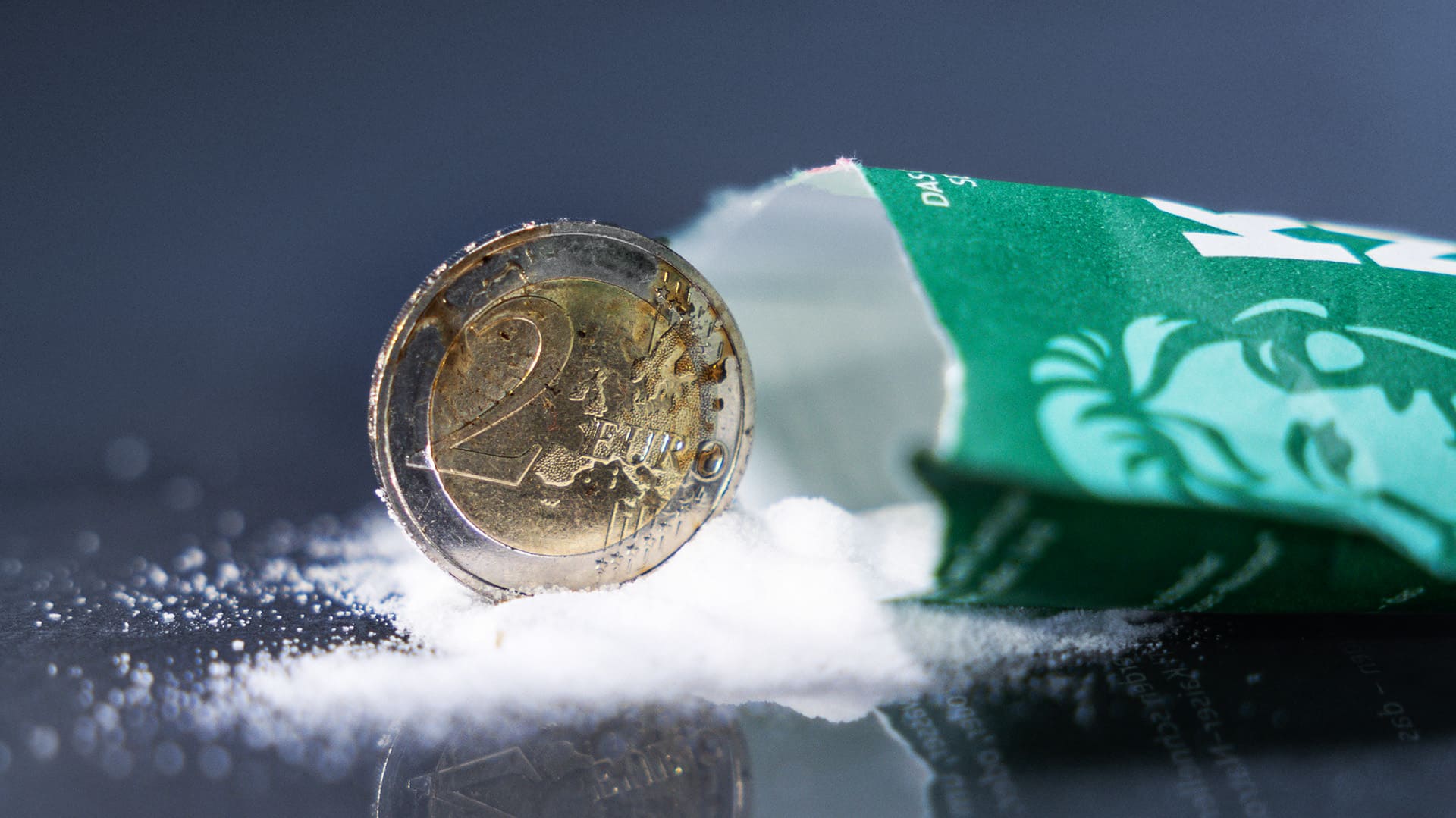 Dreckige 2-Euro-Münze steht neben offener Natronpulververpackung vor blau-grauen Hintergrund Dreckige 2-Euro-Münze steht neben offener Natronpulververpackung vor blau-grauen Hintergrund
