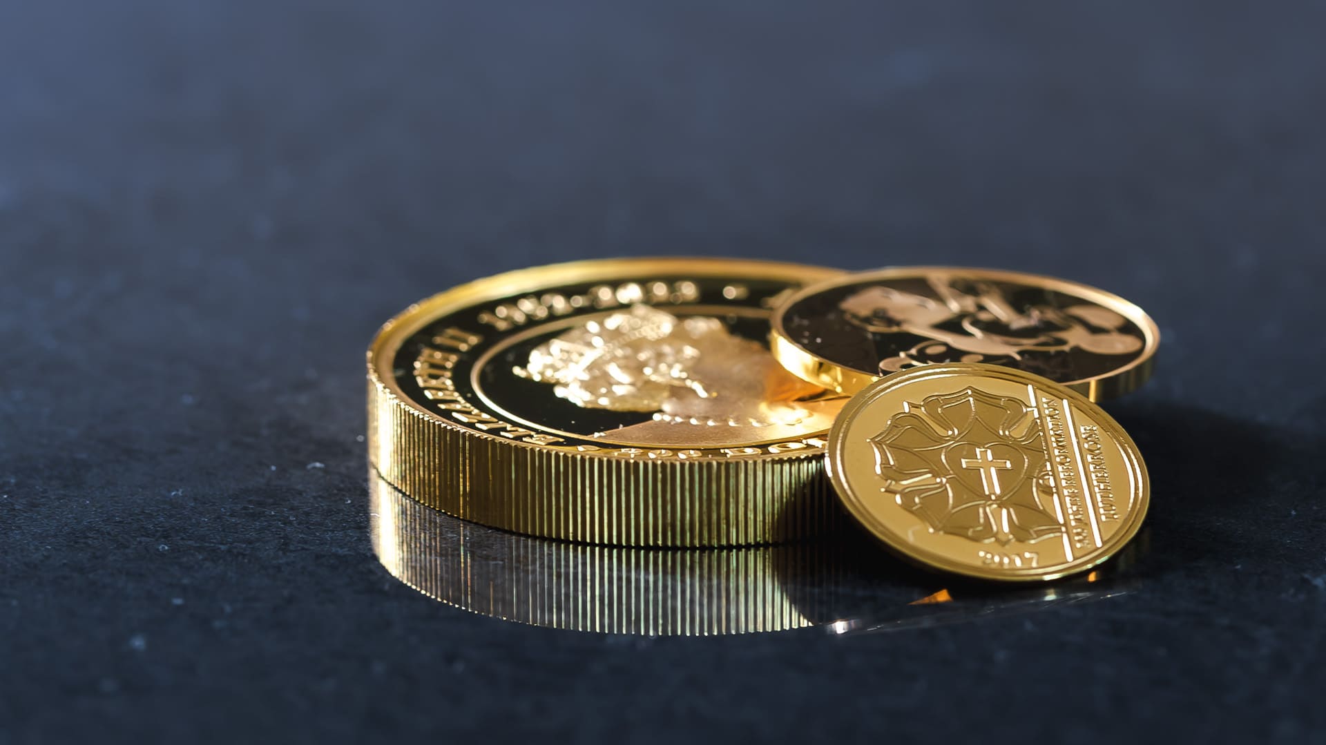 Drei Goldmünzen liegen übereinander auf blau-grauen Hintergrund Drei Goldmünzen liegen übereinander auf blau-grauen Hintergrund